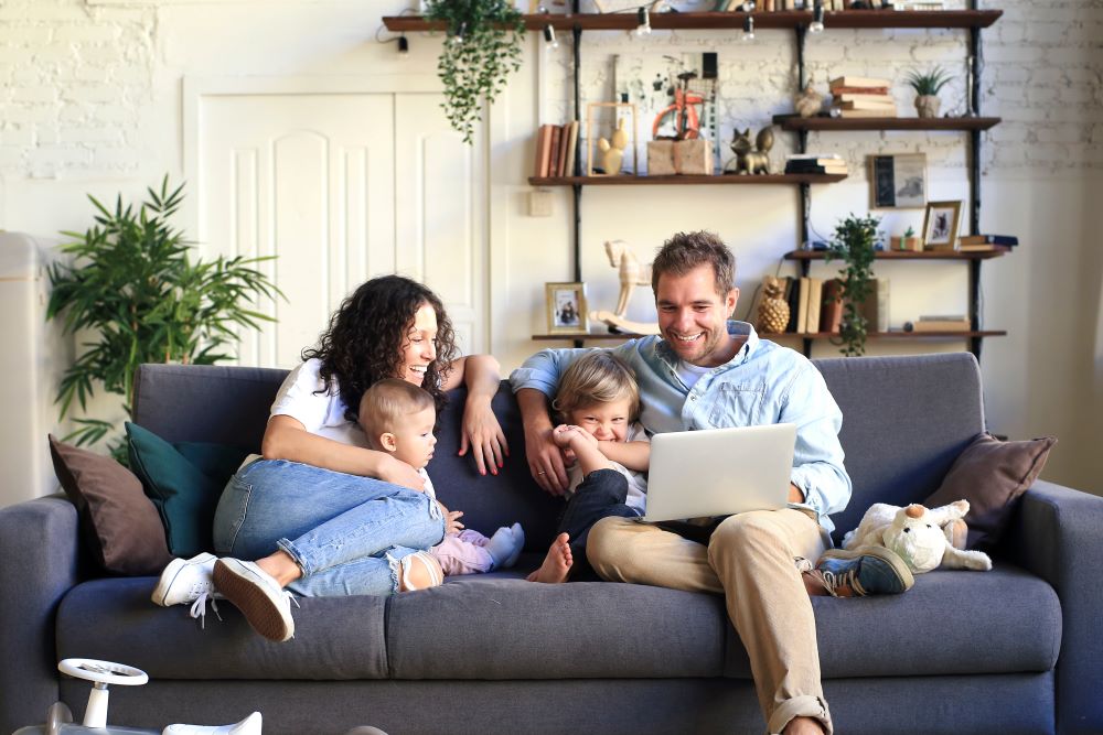 Happy family using computer on living room couch.